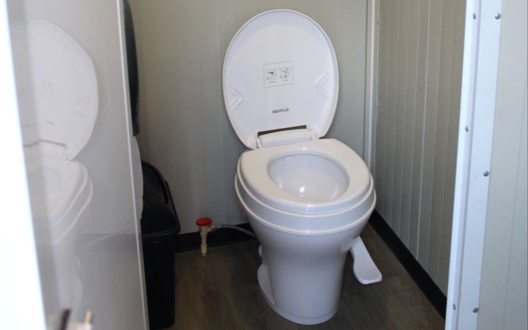 Interior del módulo sanitario SANPORT: cubículo con inodoro, piso tipo madera y ventana con ventilación natural
