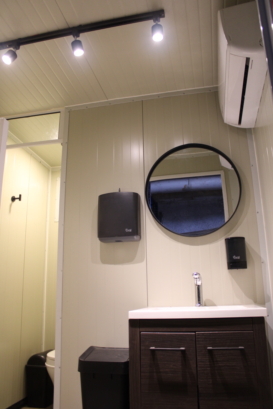 Interior premium con iluminación LED de riel, espejo redondo, lavabo con mueble de madera y aire acondicionado