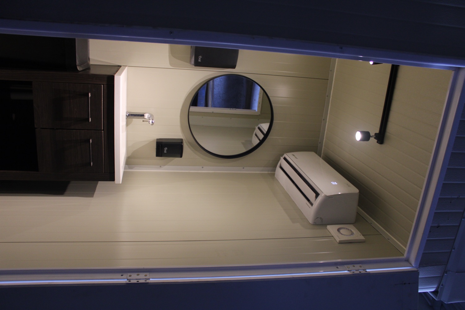 Lavabo con mueble oscuro, espejo redondo y aire acondicionado, vista interior